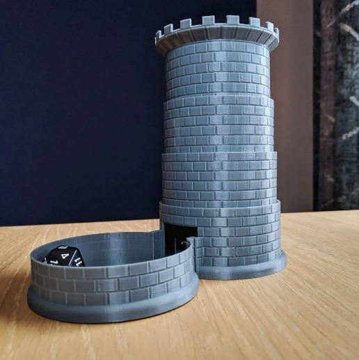 A grey 3D printed castle-shaped dice tower featuring a folding base with a black die inside.