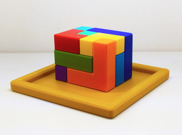 A brightly colored, interlocking 3D-printed block puzzle resting on a yellow square tray. 