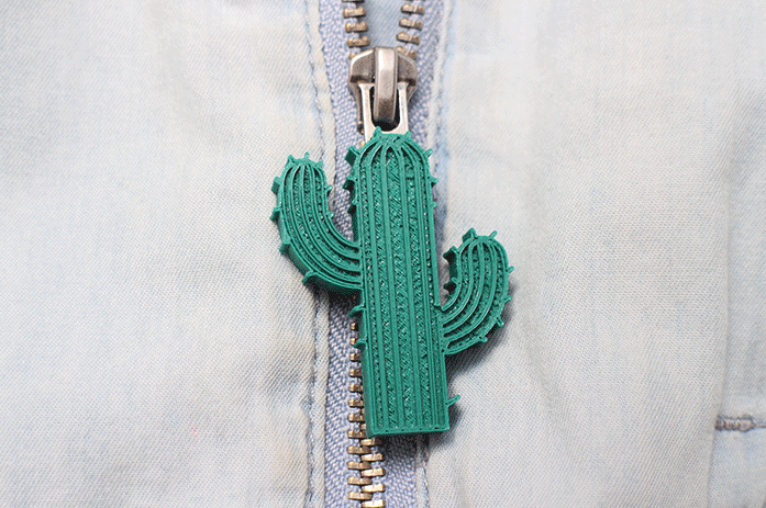 Green 3D-printed cactus-shaped zipper puller attached to a denim jacket.