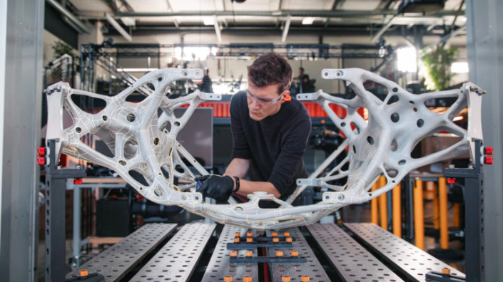 An engineer in a workshop inspecting a large, complex metal structure created using AI-driven generative design.