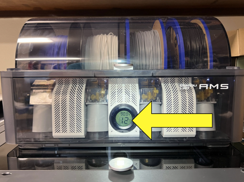 A pile of purged filament strings, often referred to as 'filament poop', gathered next to a Bambu Lab 3D printer after a multi-color print job.
