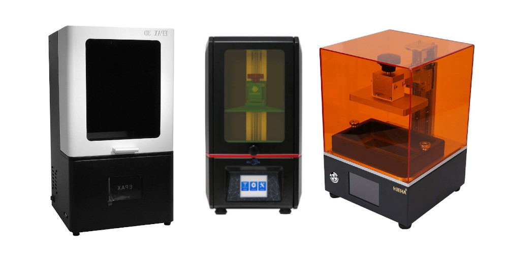 Three different desktop SLA resin 3D printers lined up side-by-side, featuring black bases and orange or dark UV-protective acrylic covers.