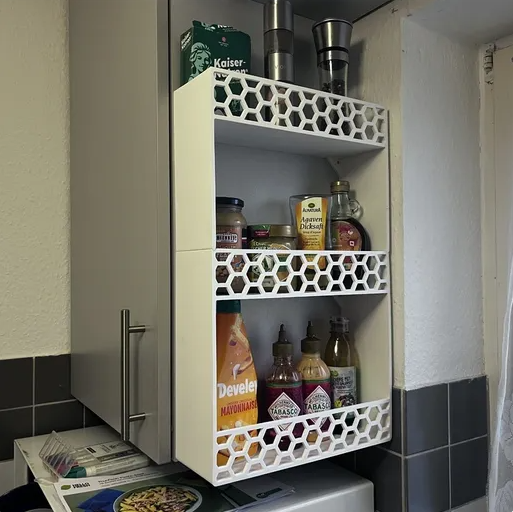 A white 3D printed wall-mounted spice rack with a honeycomb border, holding various kitchen condiments.