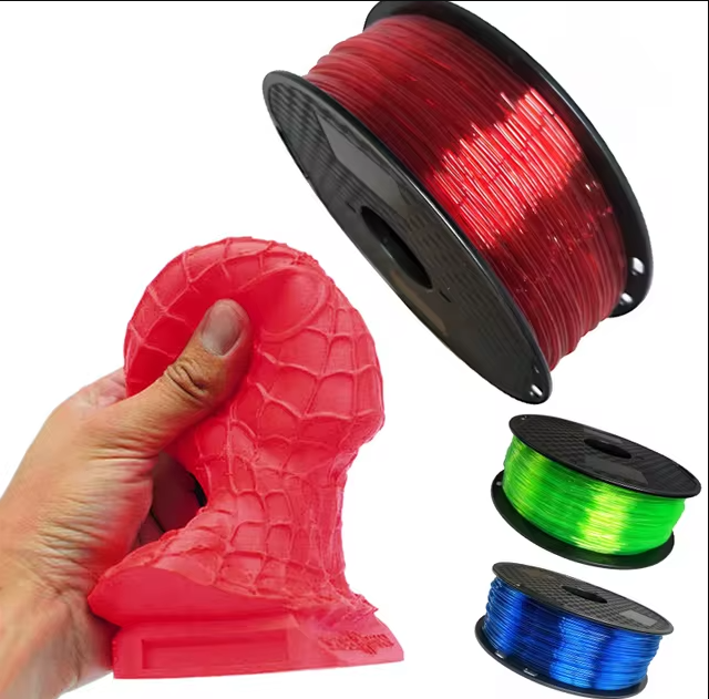 A hand squeezing a flexible, red 3D printed Spiderman bust alongside spools of green, blue, and red TPU filament.