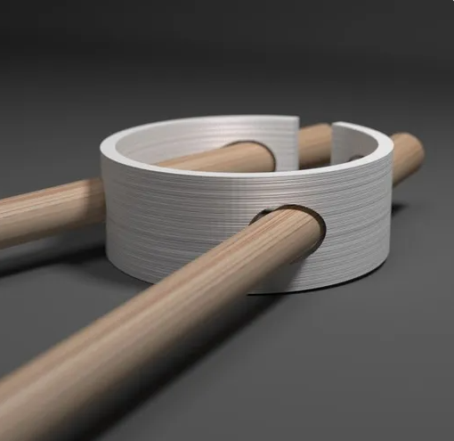 A close-up of a flexible, white, circular 3D-printed training aid keeping two wooden chopsticks perfectly aligned.