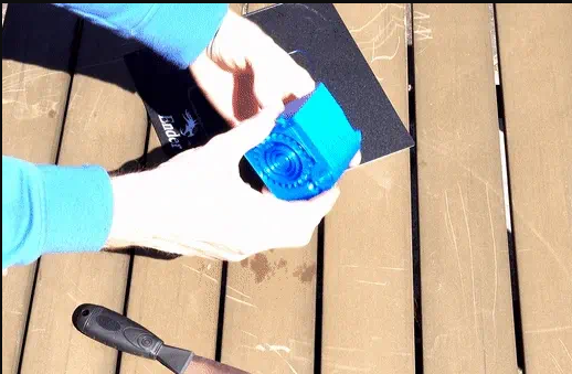 A pair of hands opening a bright blue 3D-printed spring-loaded box outdoors over a slatted wooden patio table.
