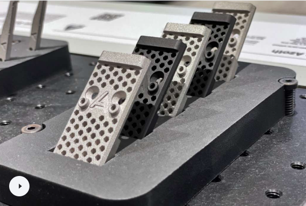 Several small, rectangular 3D printed metal components made from difficult materials like cemented carbides, lined up on a black industrial build plate.