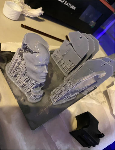 Resin 3D printer with an orange UV cover showing a complex grey 3D printed model successfully attached to the build plate