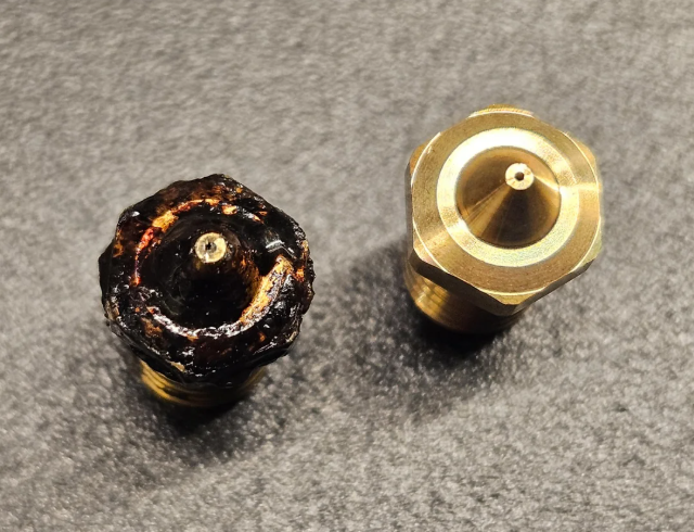 A side-by-side comparison of a clean, new brass nozzle and a heavily degraded, clogged nozzle covered in burnt plastic.