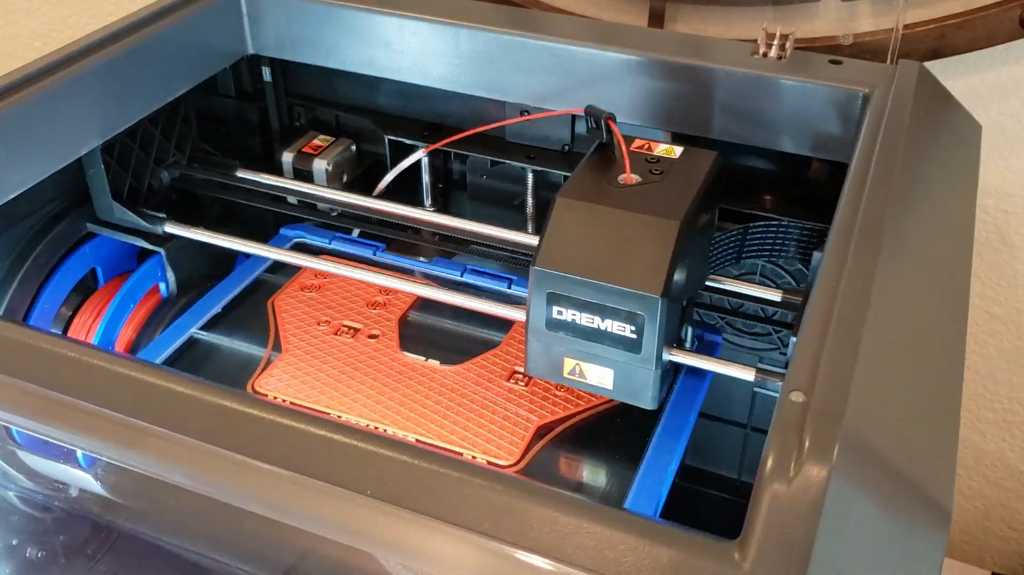 An enclosed Dremel FDM 3D printer actively printing the base layer of an orange plastic casting mold.