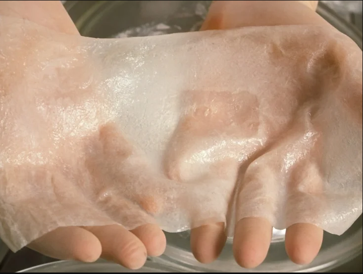 A pair of hands gently holding a thin, translucent sheet of lab-grown or bioprinted medical tissue.