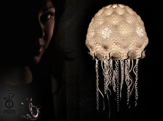 A glowing 3D printed jellyfish lampshade with intricate, textured patterns and dangling chain-like tentacles.