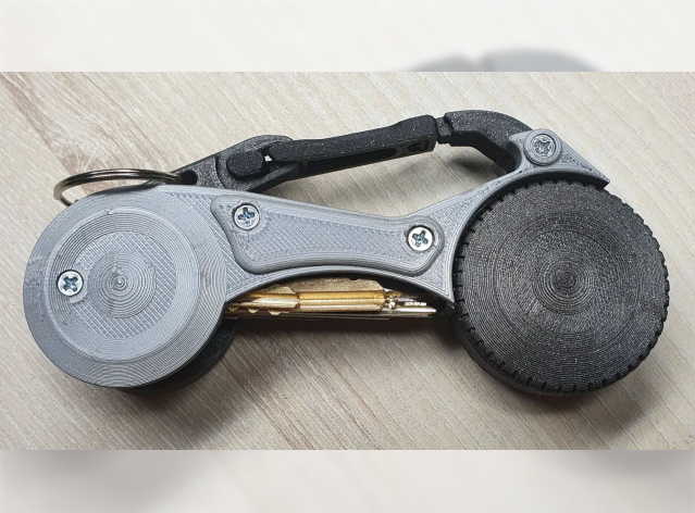 A grey and black 3D-printed key organizer equipped with a carabiner clip and a circular, hidden AirTag storage compartment.