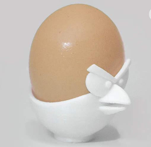 A white 3D-printed egg cup designed to look like the face of an Angry Bird, securely holding a brown boiled egg.