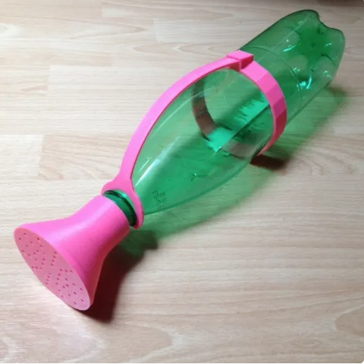 A green plastic soda bottle upcycled with a bright pink 3D-printed watering spout and carrying handle attachment