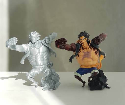 A side-by-side comparison of an unpainted grey 3D print and a fully painted model of Monkey D. Luffy striking a dynamic battle pose.