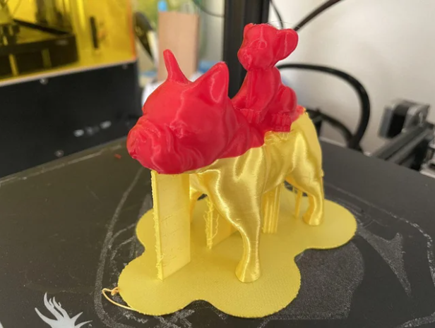 A 3D printed model of a French bulldog featuring a seamless mid-print filament change, with a bright yellow bottom half and a vibrant red top half.
