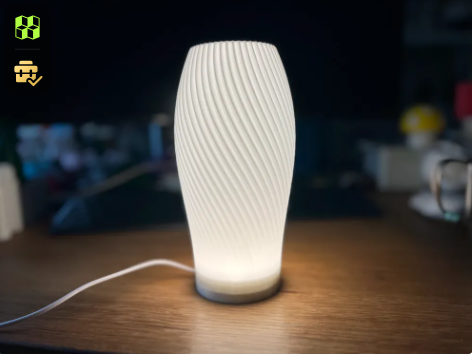 A sleek, minimalist white 3D printed lampshade with a subtle twisted texture, housing an LED lamp kit on a desk