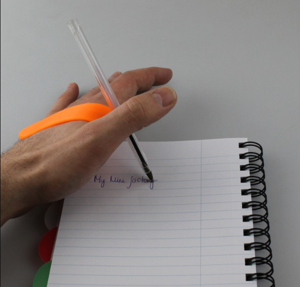 Hand writing with a pen secured by an orange 3D-printed holder.