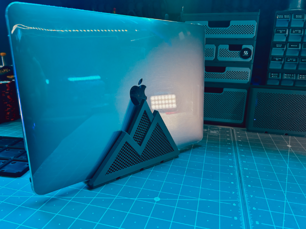 A laptop stored vertically in a rugged, mountain-shaped 3D-printed holder that is compatible with the modular Gridfinity storage system.