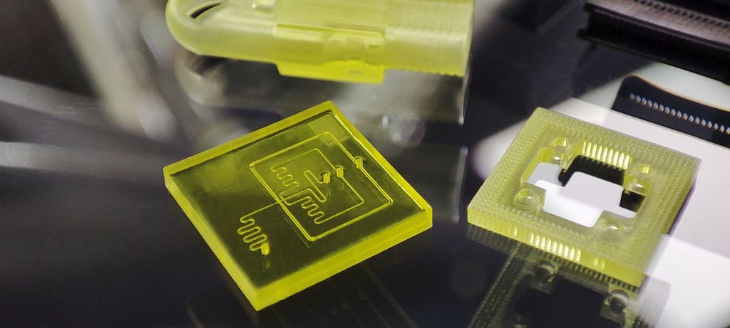 Close-up of translucent, yellow 3D printed microfluidic chips showcasing intricate internal channels for microscale fluid manipulation.