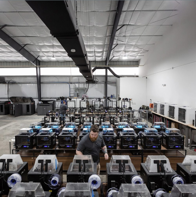 Technician monitoring rows of desktop 3D printers in an industrial print farm