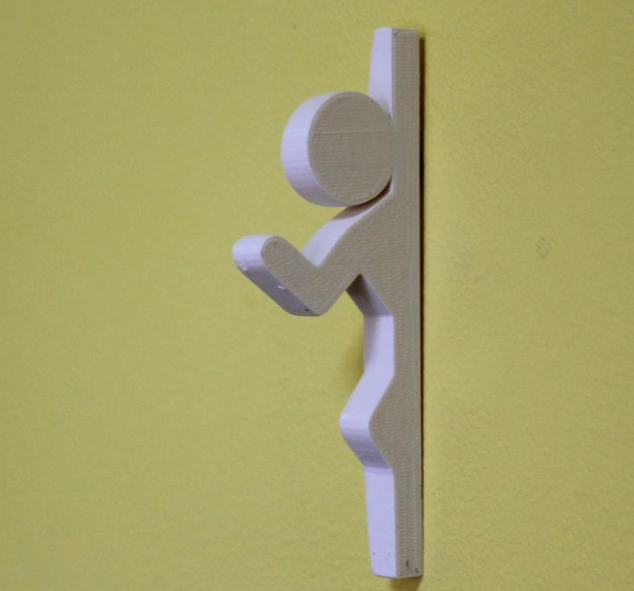 A creative white 3D printed coat hook shaped like a stick figure from the video game Portal, mounted on a yellow wall.