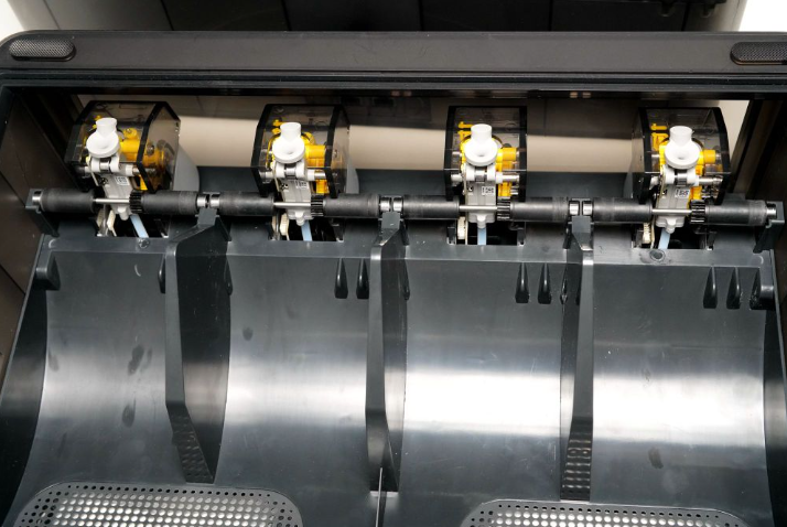 The Bambu Lab AMS Hub mechanism mounted on the back of a 3D printer, combining four separate filament PTFE tubes into a single extruder pathway.