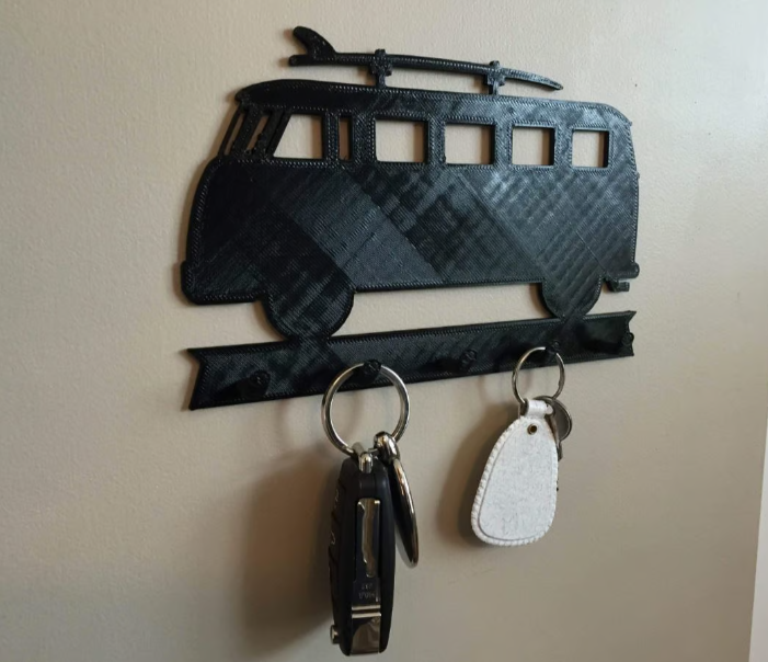 A black 3D-printed, wall-mounted key hanger shaped like a classic vintage Volkswagen bus with a surfboard on the roof.