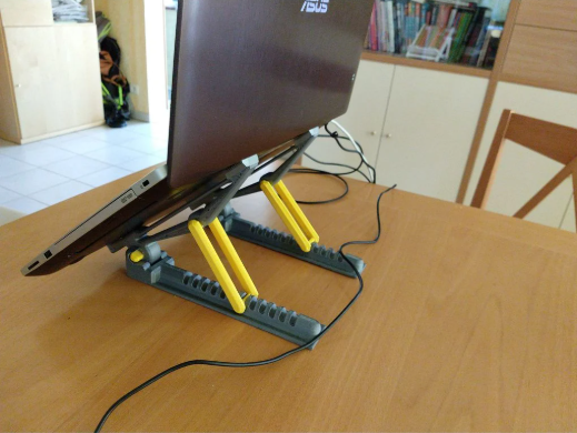A repositionable 3D-printed laptop stand featuring movable yellow hinges, designed to adjust viewing angles for users switching between sitting and standing.