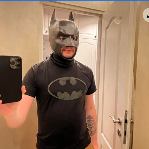 A selfie of a person wearing a 3D-printed Batman cowl mask and a Batman t-shirt, showcasing a community design from Thingiverse