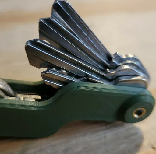 A close-up of an olive green 3D-printed minimalist key organizer neatly holding a stacked set of house keys.