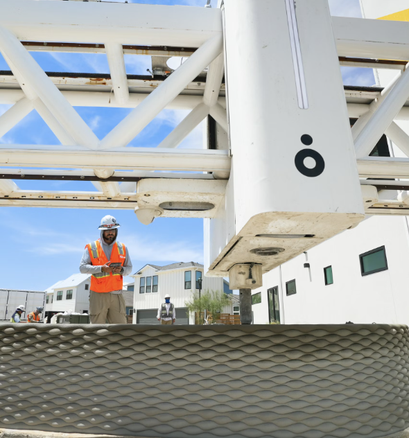 A massive ICON 3D printer extruding layers of concrete to build a home while construction workers monitor the process.  