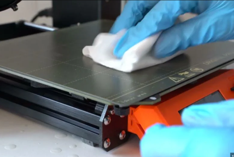 A person using a piece of paper as a feeler gauge to manually adjust the thumb screws and level a 3D printer bed.