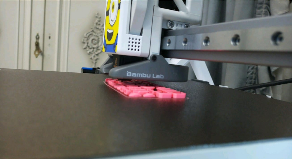 The Bambu Lab A1 3D printer actively printing a flat pink object. 