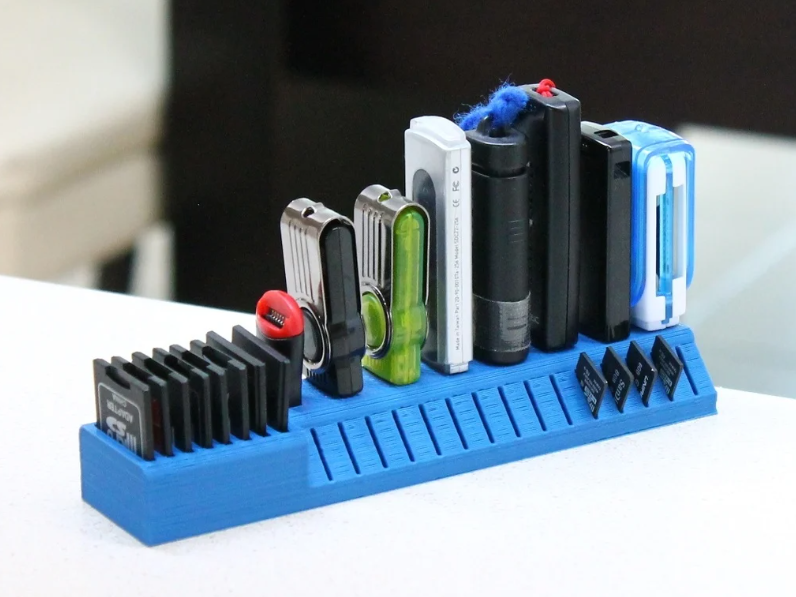 A bright blue, multi-tiered 3D printed storage organizer holding a varied collection of USB sticks and memory cards on a flat surface.