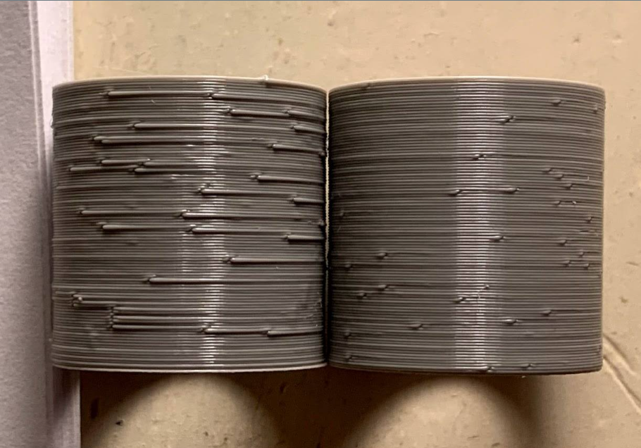 Two grey 3D-printed cylinders placed side-by-side to demonstrate the Z-seam effect; the left cylinder shows severe surface blobs and scarring, while the right shows a slightly cleaner finish.