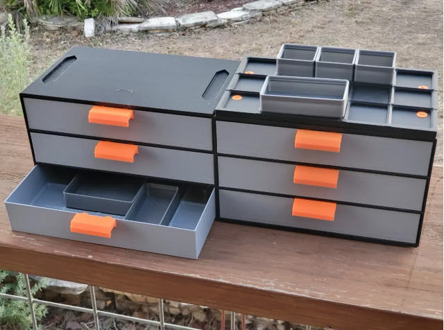 A comprehensive grey and black 3D-printed Gridfinity storage unit featuring stacked drawers with bright orange handles and customizable drop-in tray inserts.