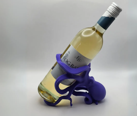 A playful purple 3D printed octopus figure sitting on a table, using its curved tentacles to securely cradle a bottle of white wine