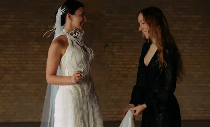 A fashion model wearing an intricate, avant-garde white 3D-printed dress demonstrating the intersection of fashion design and additive manufacturing.