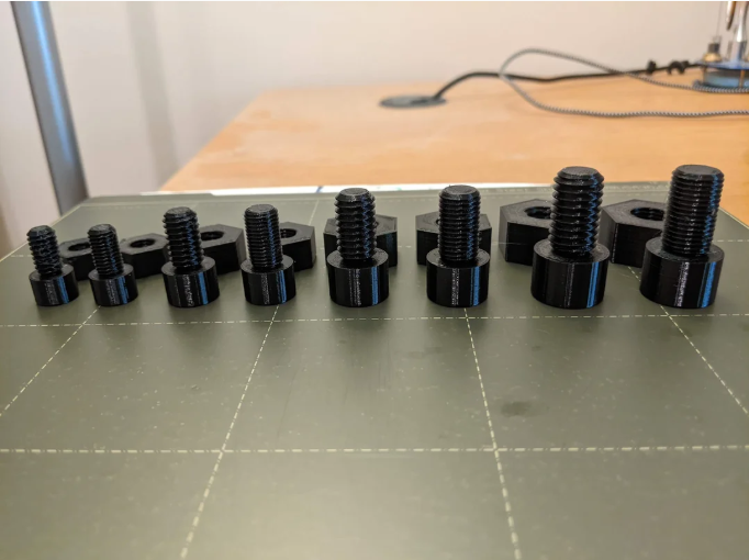 A collection of functional, black 3D printed screws and hex nuts of varying sizes resting on a build plate