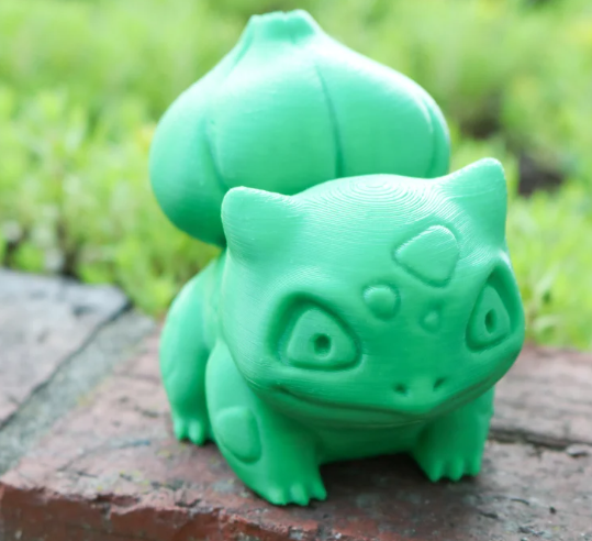 A smooth, green, high-poly 3D printed Bulbasaur figurine sitting on an outdoor brick surface.