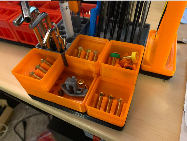 A close-up view of vibrant orange 3D-printed Gridfinity bins perfectly organizing small brass 3D printer nozzles, screws, and assorted workbench tools.