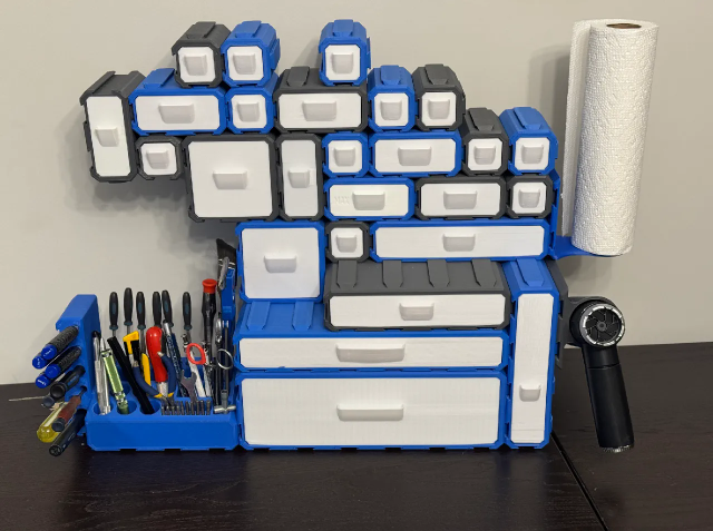 A blue and white 3D printed modular desk organizer featuring multiple small drawers, tool holders for pliers, and a paper towel roll attachment.