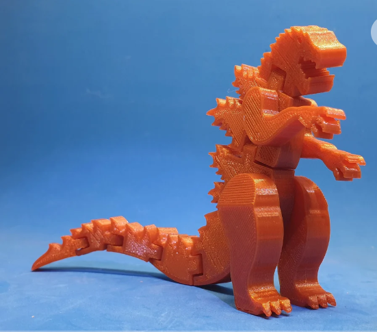 A bright orange, fully articulated 3D printed Flexi Godzilla toy showcasing its movable tail, arms, and legs.