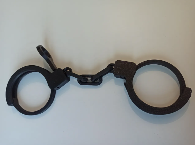 A pair of functional 3D-printed black handcuffs featuring a print-in-place working locking mechanism and a small matching key
