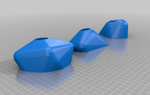 A 3D digital render of three blue, multi-faceted climbing holds of varying sizes arranged in a row on a grey grid surface