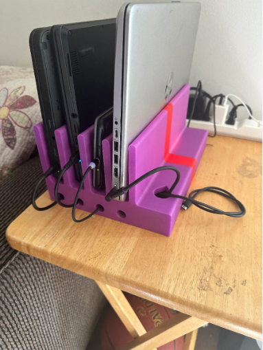 A purple and red 3D-printed vertical charging station organizing multiple laptops and tablets with built-in cable routing channels.