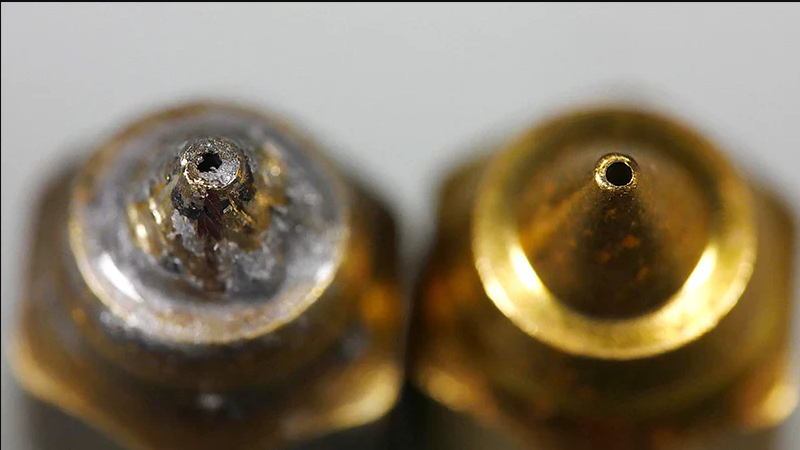 Side-by-side comparison of a heavily worn brass 3D printer nozzle next to a brand-new, clean brass nozzle.