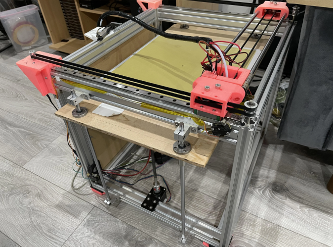 Top-down view of a CoreXY 3D printer frame highlighting the pink printed parts, belts, and dual-motor pulley system